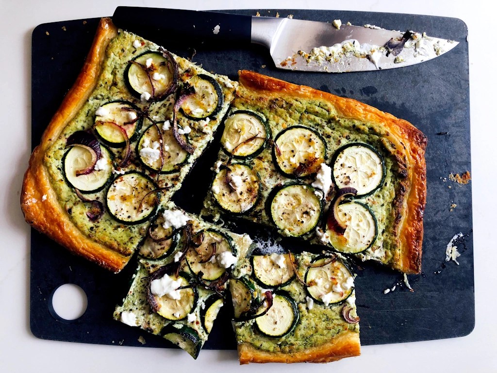 Overhead shot of courgette pesto flatbread on a cutting board with knife
