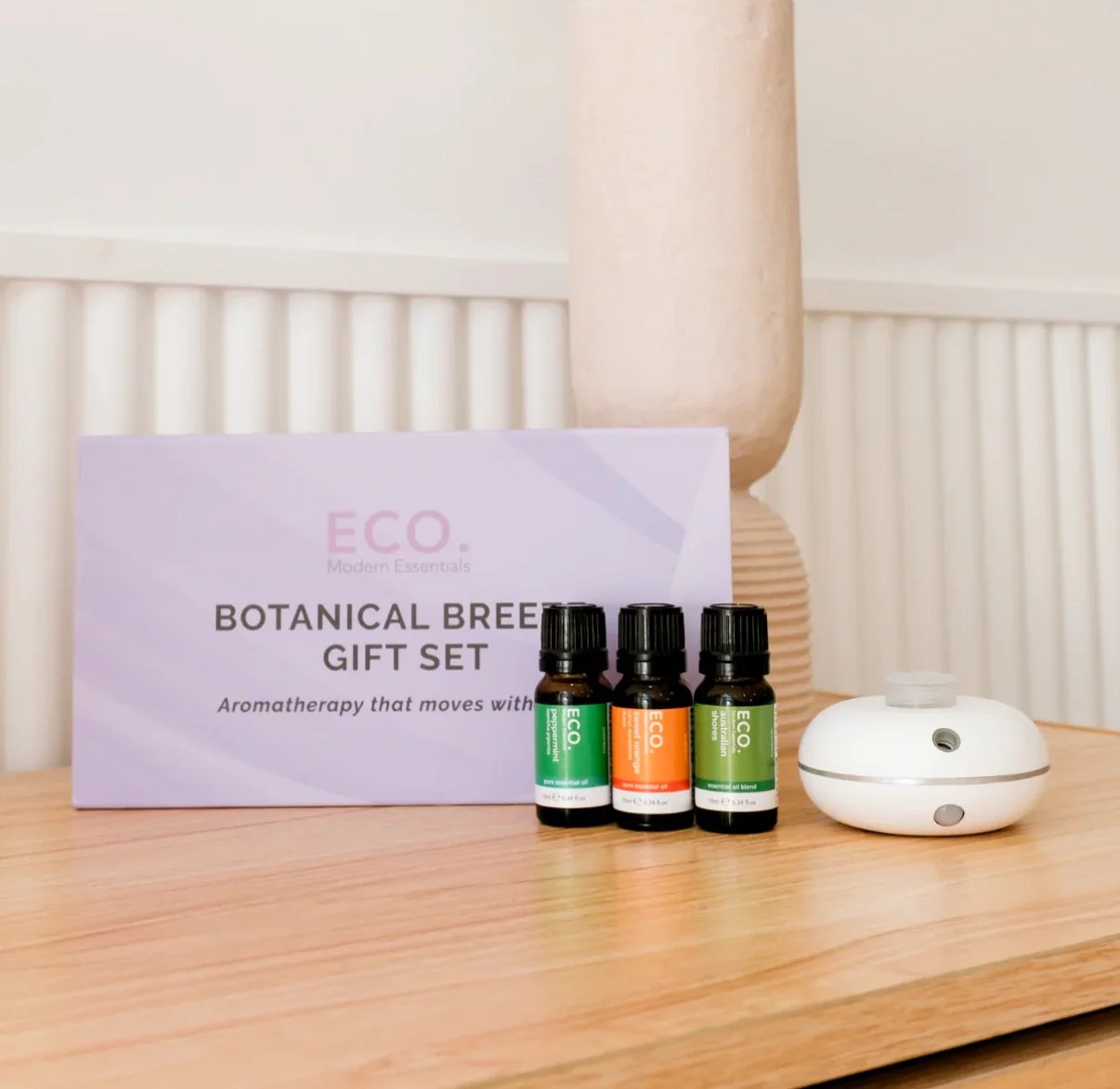 The Botanical Breeze Gift Set features a motion sensor diffuser and three essential oils, elegantly displayed on a wooden surface in a softly lit room.