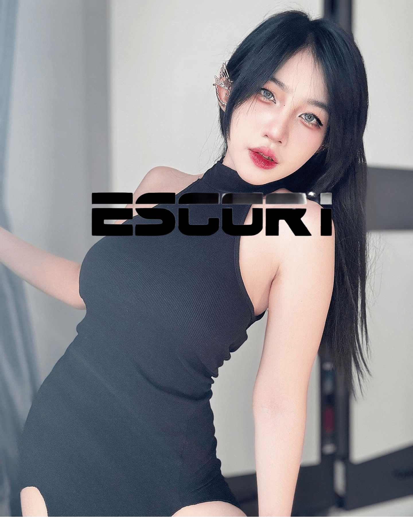 Portrait of a woman with long black hair wearing a black sleeveless top, looking at the camera with soft makeup.