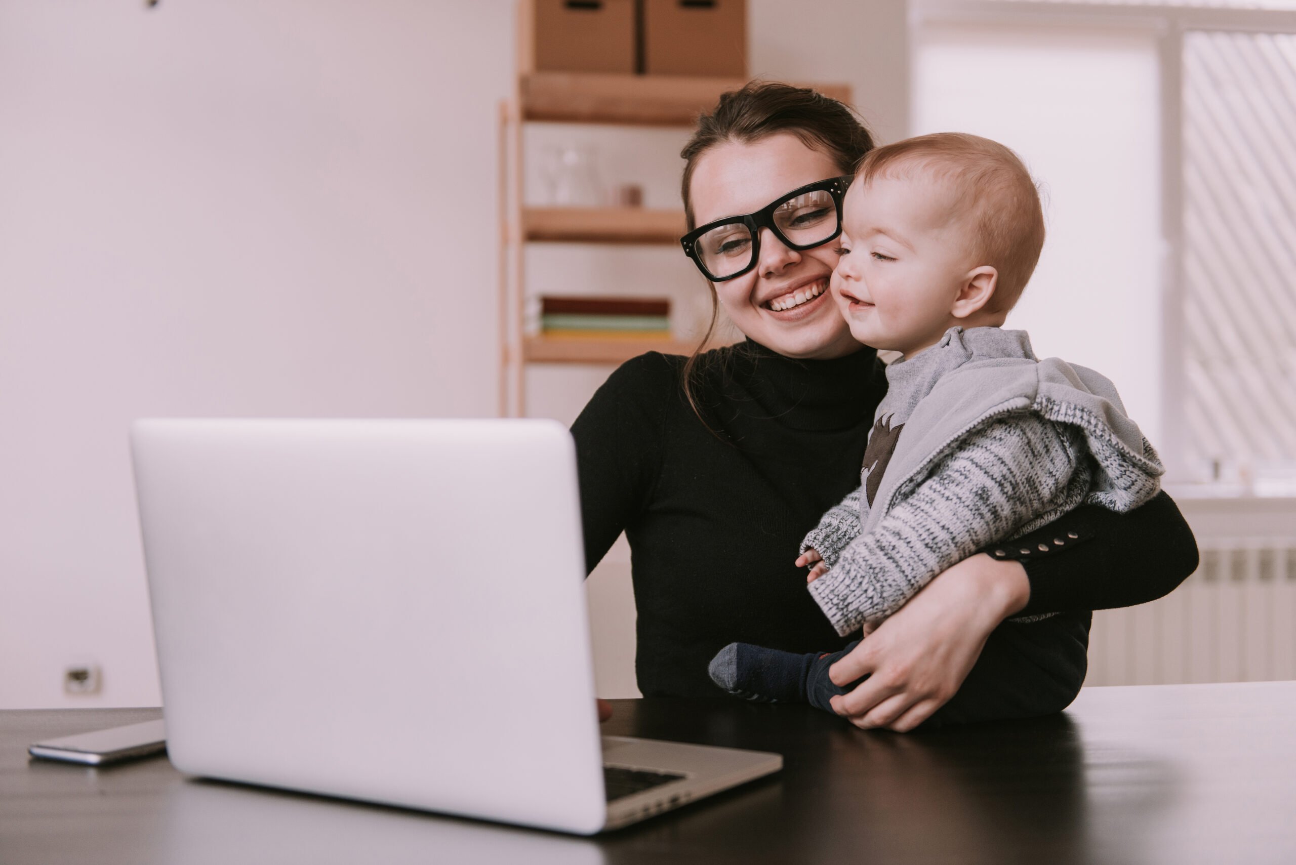 Young,Mother,Working,At,Home,With,Laptop,Holding,Her,Little