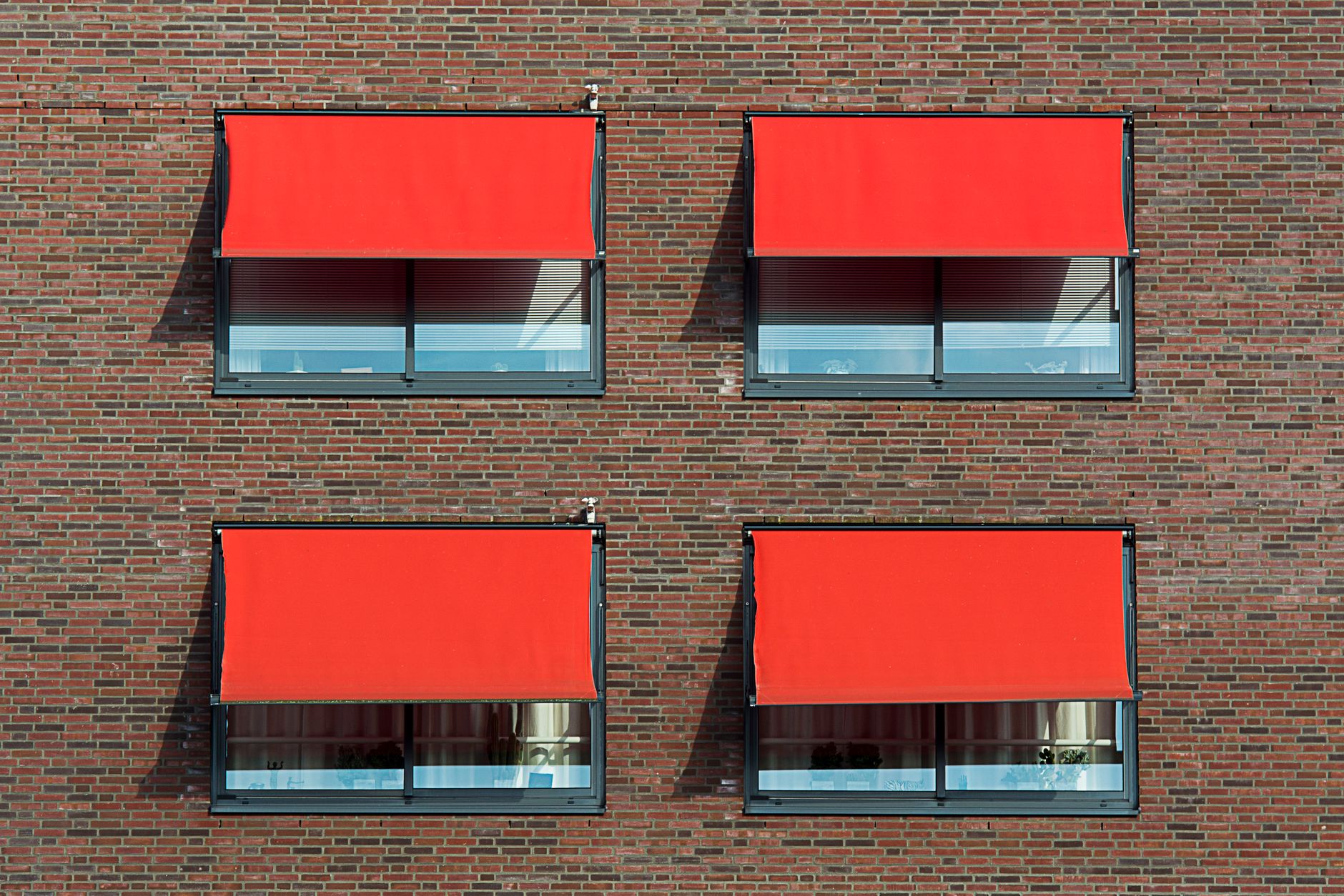 a brick wall with red sun shades on glass windows