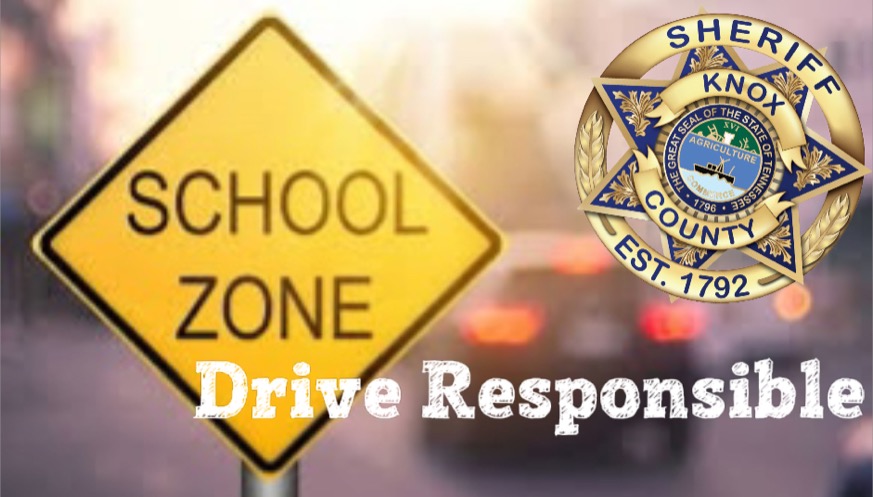 School Zone sign with KCSO badge and "Drive Resposibly" and blurred car brake lights