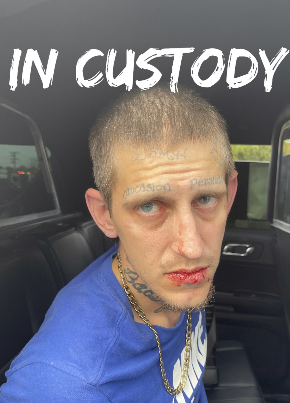 Man with face tattoos in back seat and "In Custody"