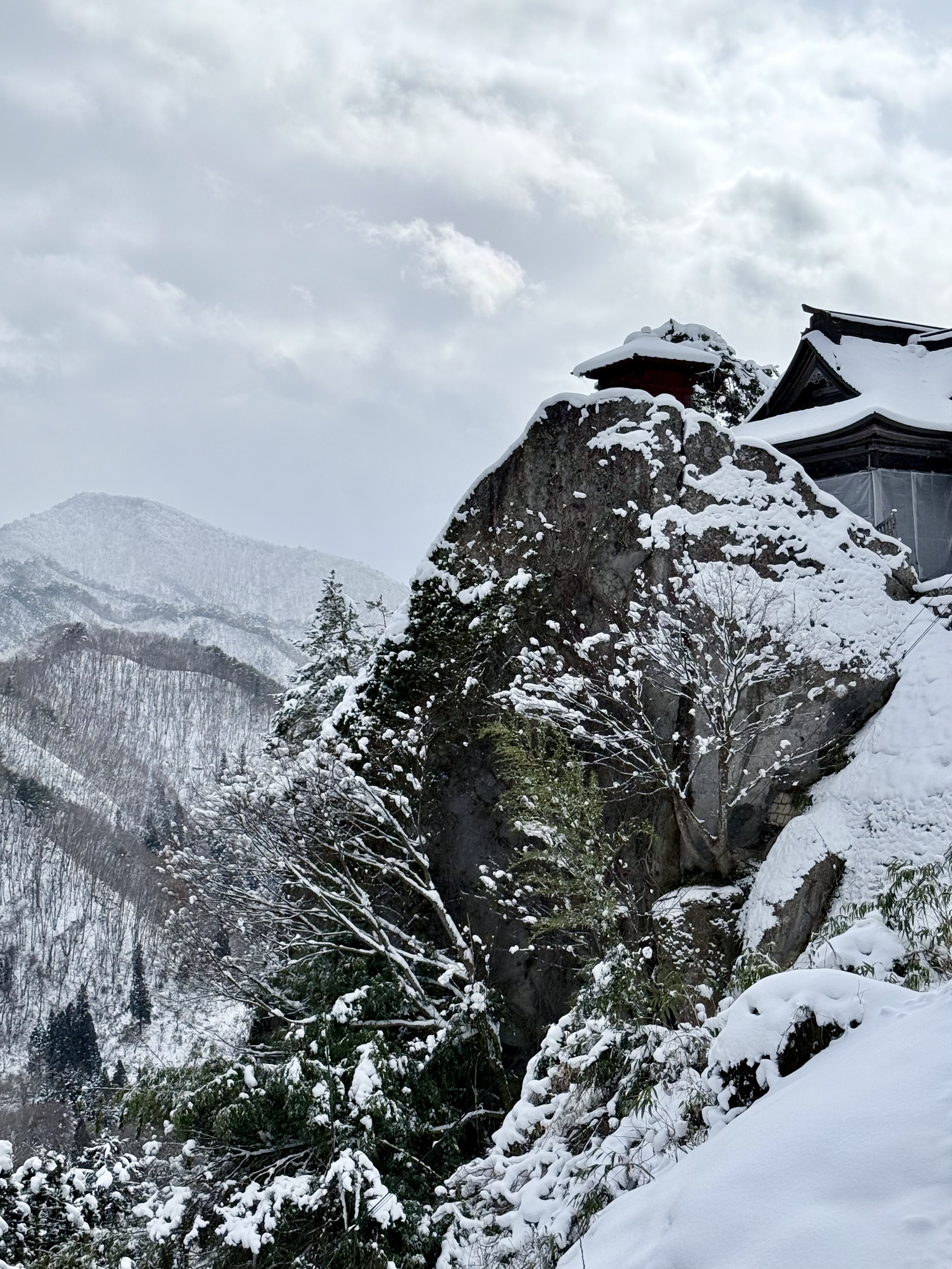 Snow-covered mountainside with a rocky outcrop and a pagoda-style temple roof perched on the cliff.