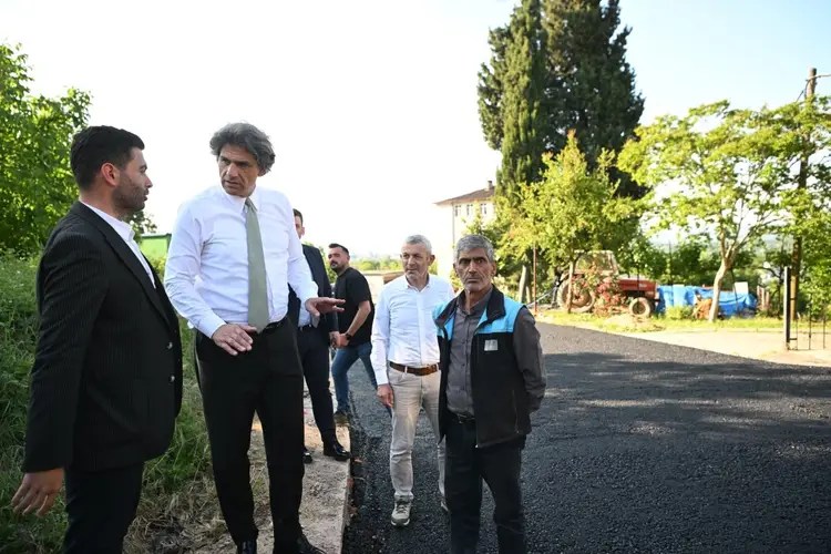 Kartepe Belediyesi yetkilileri bir yolda asfalt serim sürecini değerlendiriyor. Beş kişi, yeni asfalt dökülmüş yolda bir araya gelmiş.