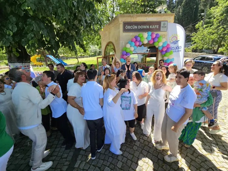 A joyful group of diverse individuals celebrating outside a café with a festive atmosphere, surrounded by greenery and colorful decorations.