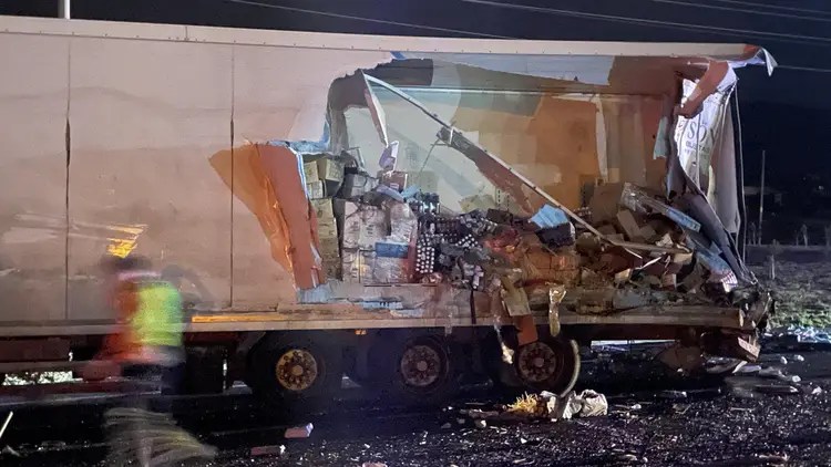 Bir tırın arka kısmında meydana gelen hasar, kazanın şiddetini gösteriyor. Tırın kasası açılmış ve içerisi dağılmış durumda. Olaya müdahale eden bir kişi görünmekte.