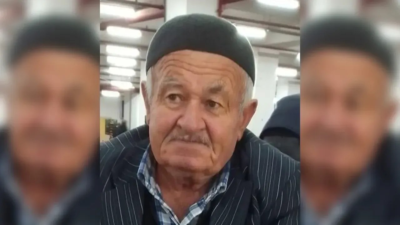 Orta yaşlı bir adam, iç mekanlarda otururken görünmekte, üzerinde düz bir şapka ve çizgili bir ceket bulunmakta.