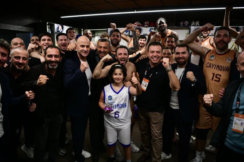 Çayırova Belediyesi basketbol takımı, galibiyet sonrası kutlama yapan oyuncular ve koçlarla dolu bir soyunma odasında, mutluluk ve zafer coşkusu içinde bir araya gelmiş.