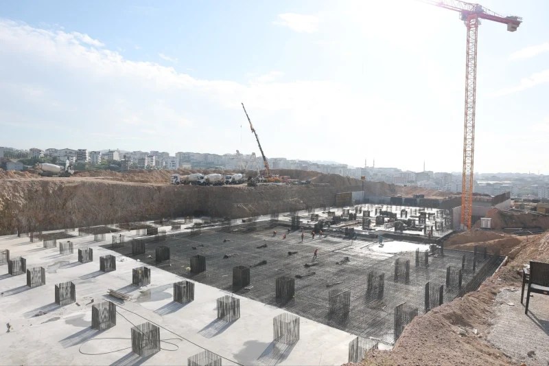 Çayırova Devlet Hastanesi inşaat alanında temel beton serimi ve yapı çalışmaları devam ediyor. Arka planda iş makineleri ve inşaat ekipmanları görünmektedir.
