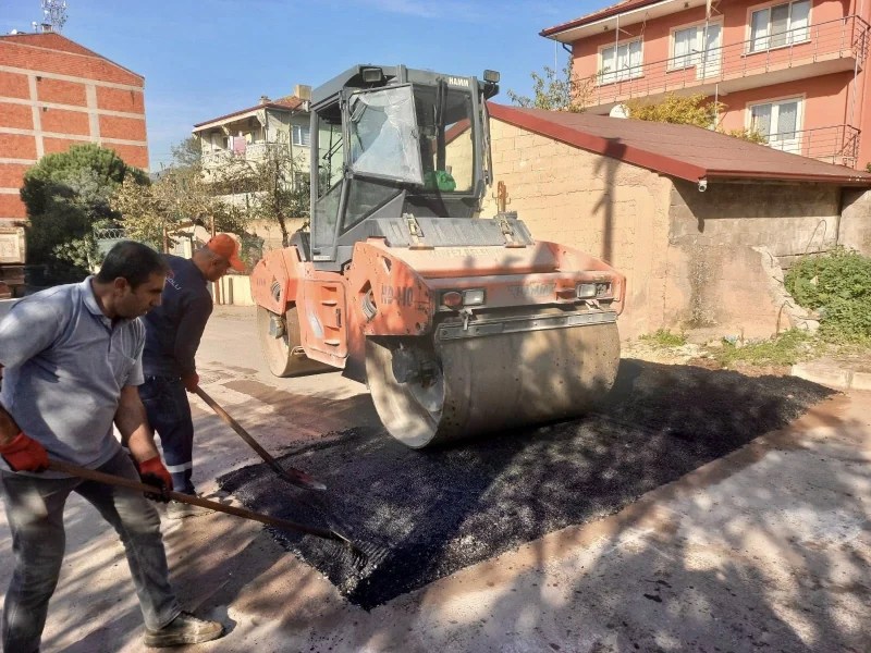 Asfalt yama çalışması sırasında bir iş makinesi ve iki görevli, yol bakım onarım işlemleri yapıyor.