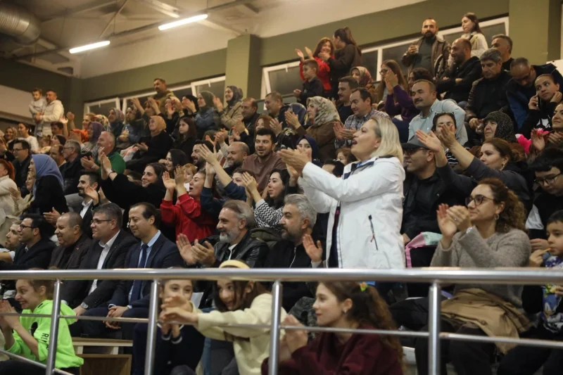 İzleyicilerin dolu bir spor salonunda öğretmenler için düzenlenen voleybol turnuvasını coşkuyla izlediği bir salon görüntüsü.