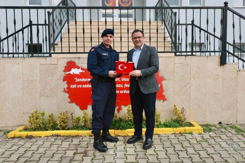 Belediye Başkanı Sertif Gökçe, İlçe Jandarma Komutanı Üsteğmen Anıl Bahadır Irkın ile birlikte Türkiye bayrağını tutuyor, jandarma binasının önünde poz veriyor.