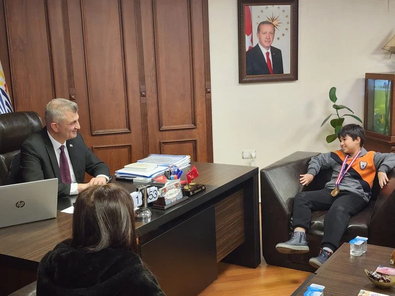 Gölcük Belediye Başkanı Ali Yıldırım Sezer, Halıdere İlkokulu öğrencisi Sarp Arel Güvenç'i makamında ağırlayarak tebrik ediyor. Sarp, matematik olimpiyatlarında üç altın madalya kazanmış. O sırada masanın yanında oturuyor.