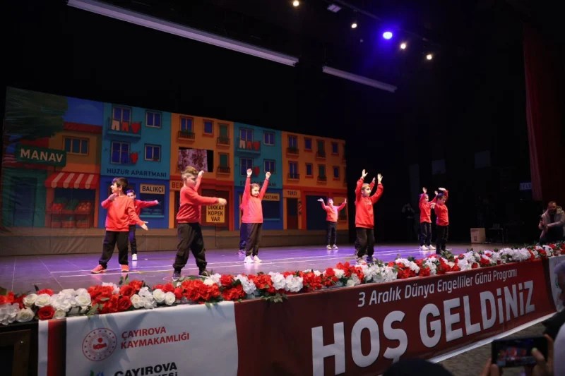 Çayırovalı özel bireyler, 3 Aralık Dünya Engelliler Günü etkinliğinde sahne alarak gösteri yapıyor. Arka planda dekoratif sahne tasarımı ve izleyiciler görülüyor.
