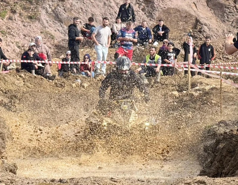 A TV racer speeding through a muddy course, creating a spray of water and mud, with a crowd of spectators in the background watching eagerly.