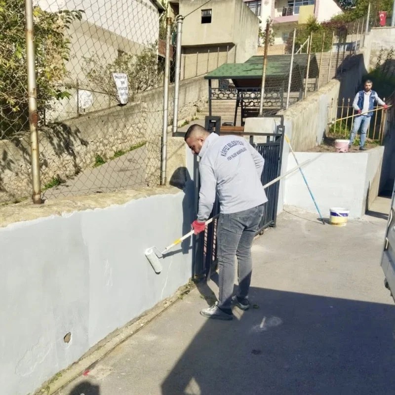 Bir çalışan, Kışladüzü İlkokulu'nun bahçe duvarını gri renge boyuyor. Etrafında başka çalışanlar ve bir sıra duvar görünmekte.