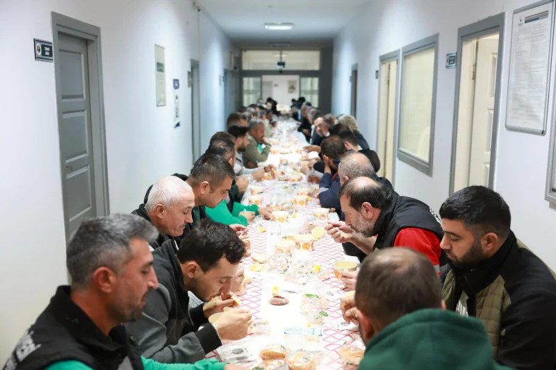 Derince Belediyesi Fen İşleri Müdürlüğü'nde gerçekleşen kahvaltı programında çalışanlar uzun bir masa etrafında oturmuş, yemeklerini yiyerek sohbet ediyorlar.