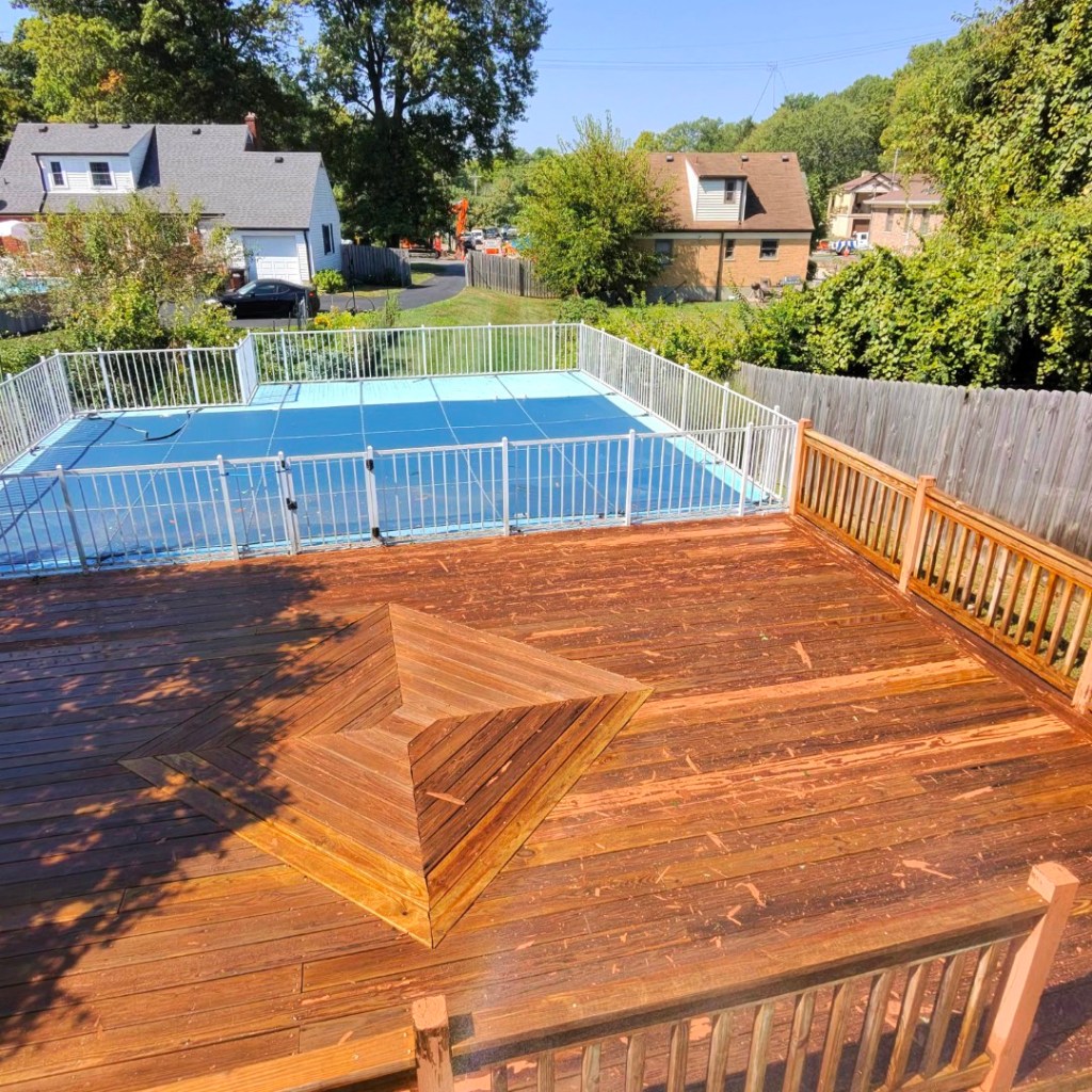 A pool deck with weathered wood and pieces of peeling behr deckover