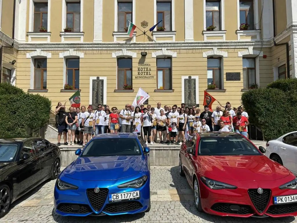 Група ученици пред общината в Котел, с две коли Alfa Romeo, флагове и усмивки на лицата.