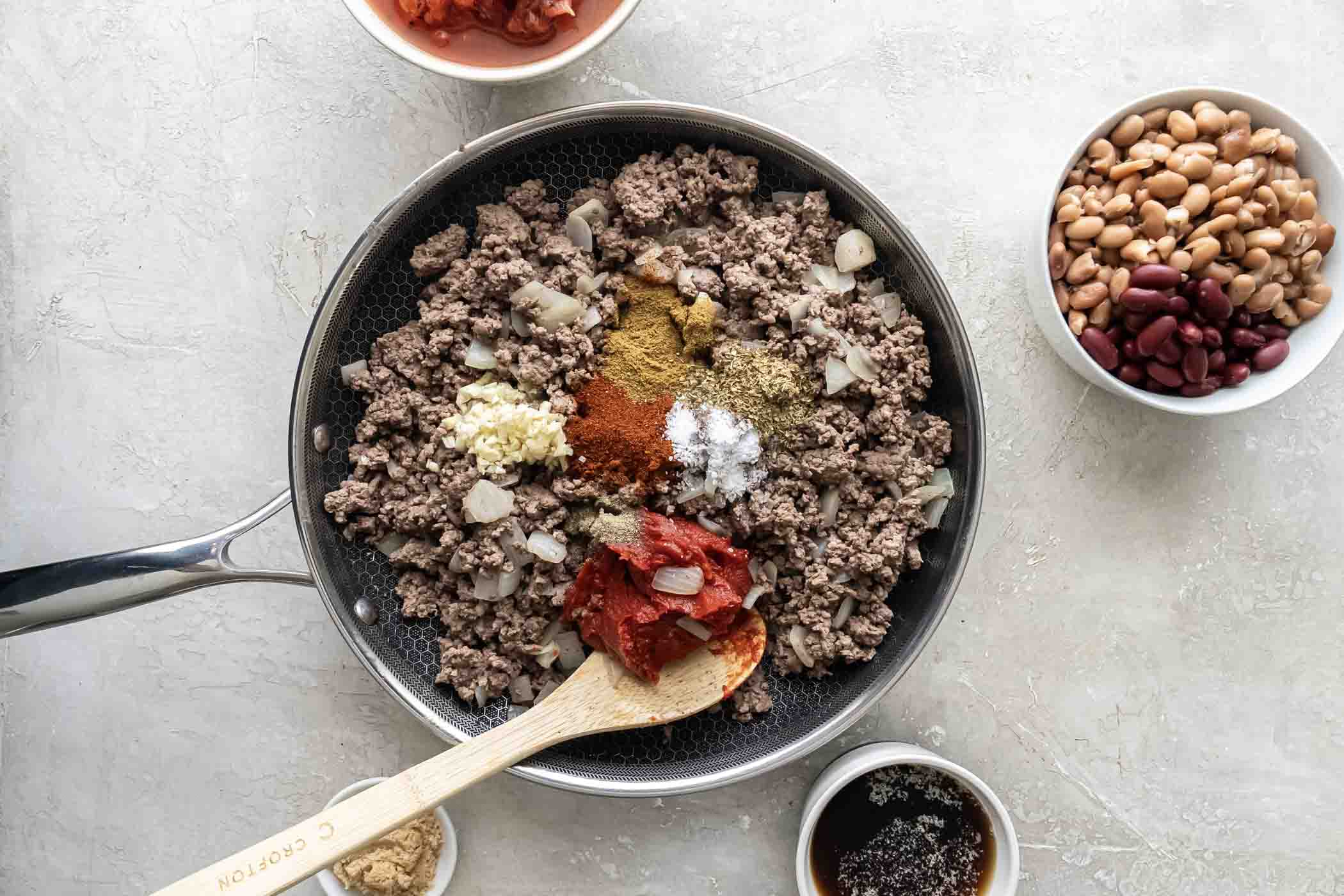 Tomato paste and spices added to browned ground beef and onion in skillet.