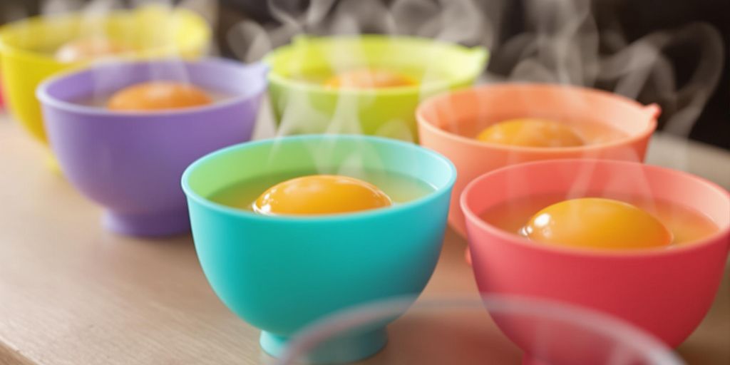 Colourful silicone egg poaching cups with poached eggs.