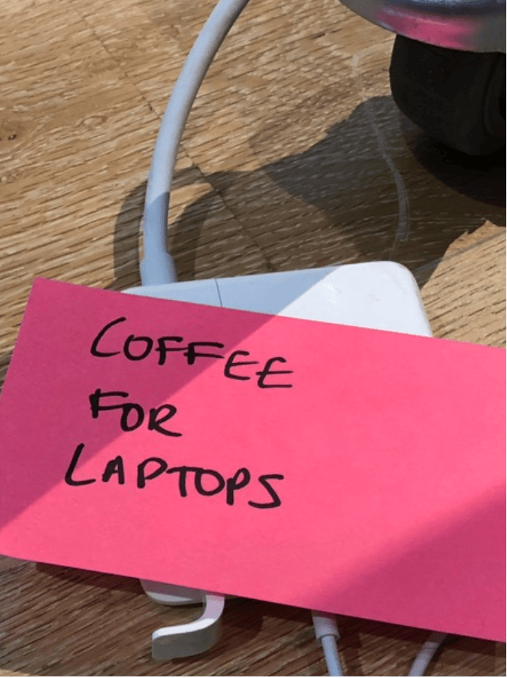 A pink sticky note reading COFFEE FOR LAPTOPS, taped to a laptop charger
