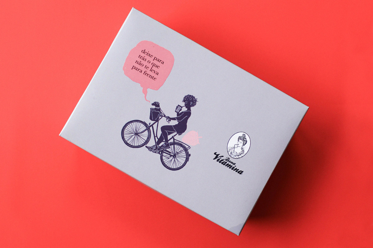 Embalagem da Dona Vitamina com ilustração de uma ciclista e balão de fala cor-de-rosa, sobre fundo coral