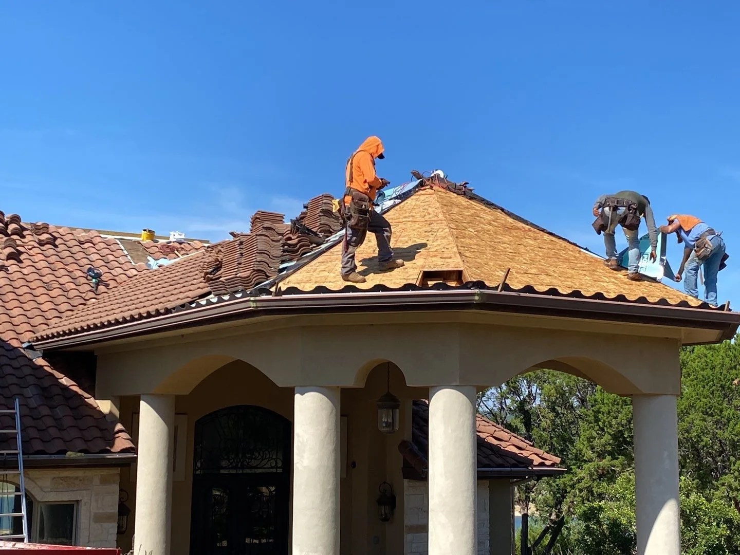 Local roofing installation crews safely repairing a premium residential tile roof on a home in Lakeway Texas