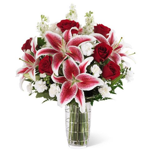 A bouquet of pink lilies, red roses, and white baby's breath in a clear glass vase.