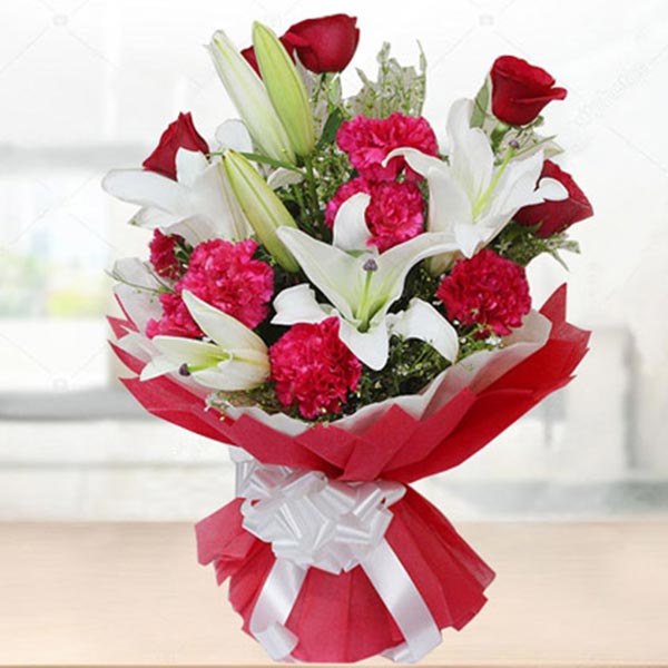 A vibrant bouquet of red roses, pink carnations, and white lilies wrapped in red and white.