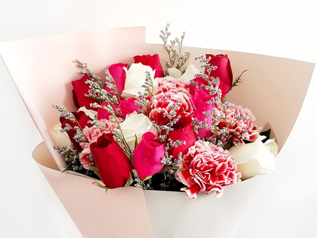 A vibrant bouquet of red, pink, and white flowers wrapped in soft paper.