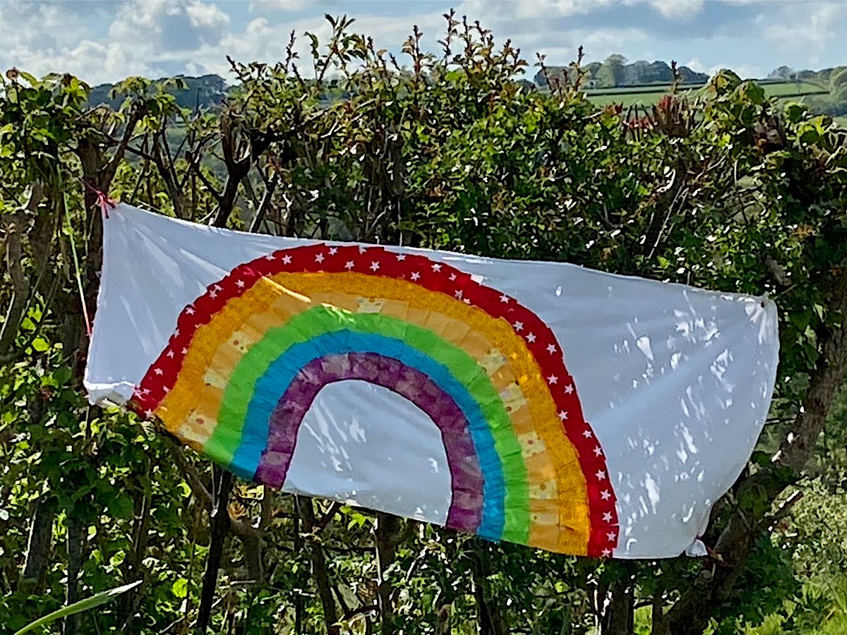 A rainbow painted onto a sheet and hung on a hedge
