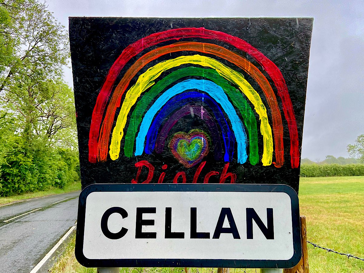 A rainbow painted on black board, says 'diolch' underneath and a small heart shaped also rainbow coloured heart sits under the rainbow. It is mounted onto the sign for Cellan