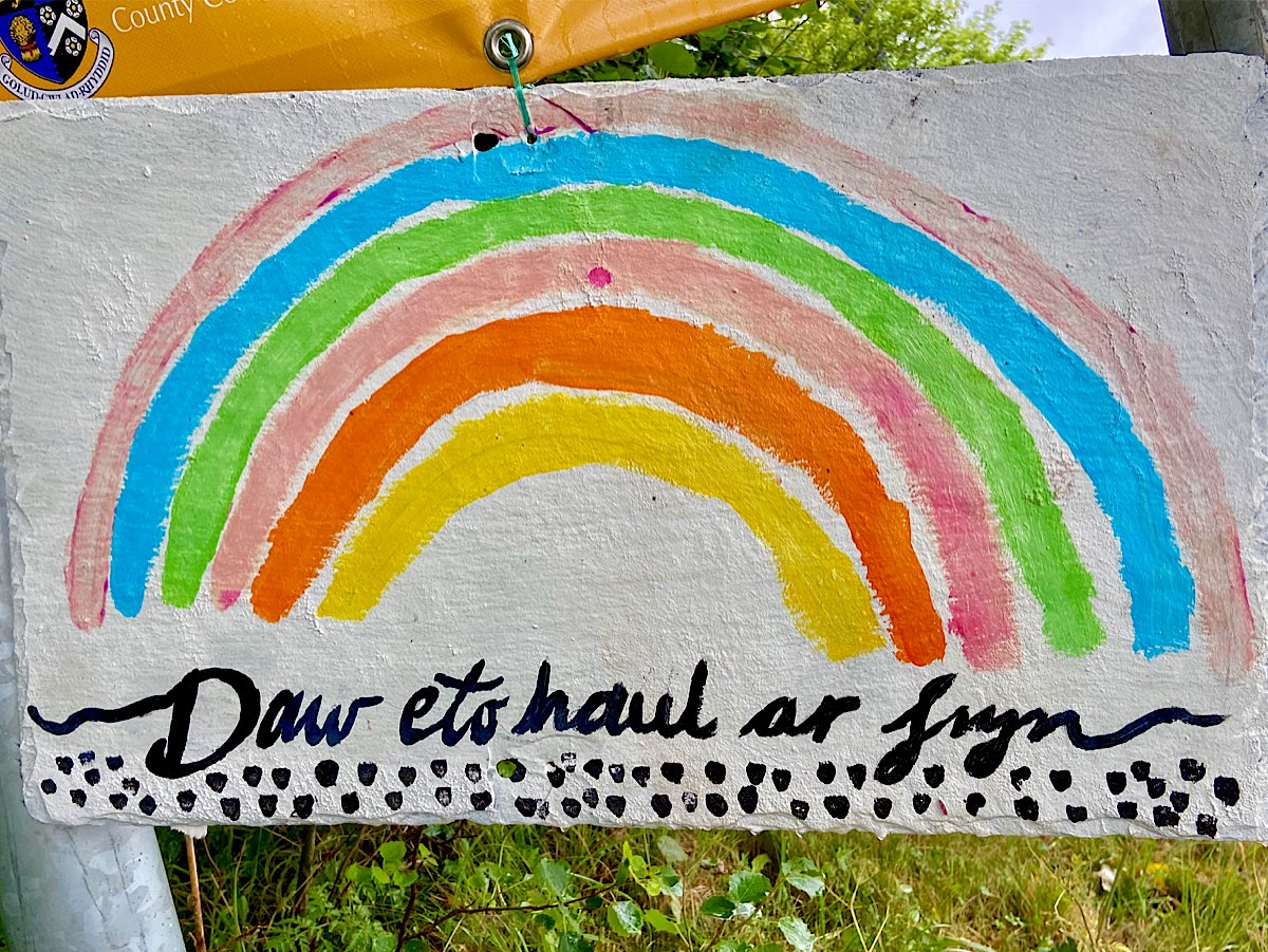A rainbow painted on white board, says 'daw eto haul ar fryn' underneath and a small heart shaped also rainbow coloured heart sits under the rainbow.