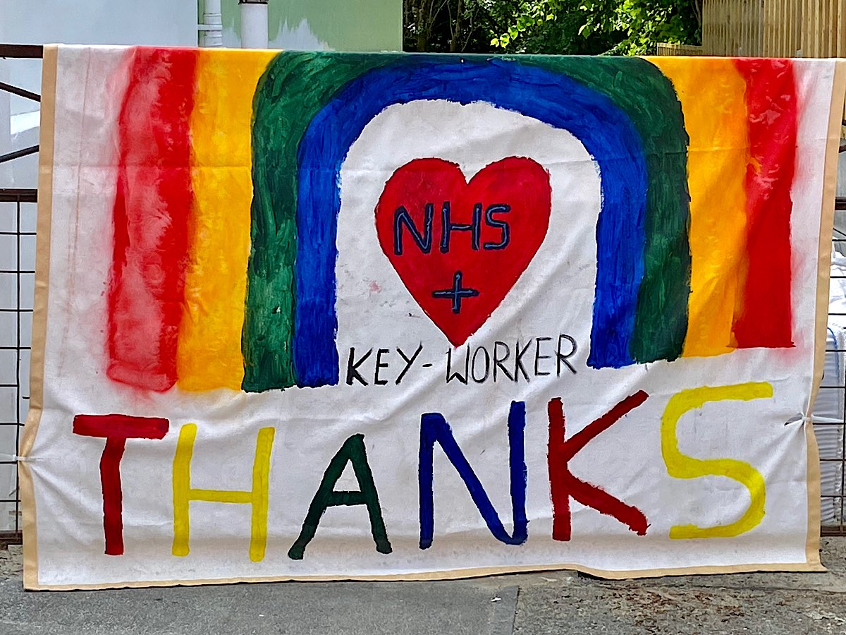 A huge painted banner hanging on a gate post, a 4 colour rainbow with a red heart in the centre that says NHS + key-worker and a huge THANKS at the bottom