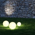 Landscape lighting design and construction webpage link thumbnail image of dark green grass and a grey and beige stone wall with small illuminated white orb lights on the grass in the foreground