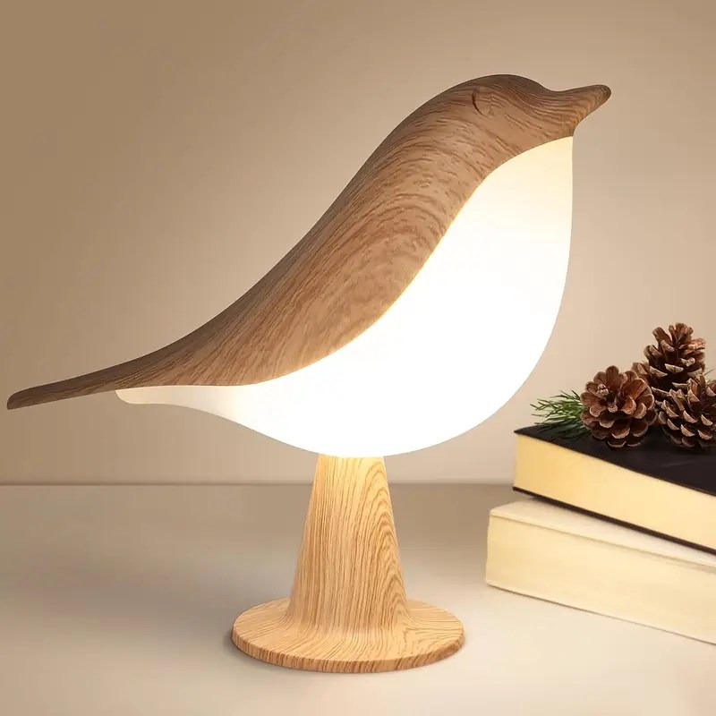Warm glowing wooden bird lamp on bedside table with books and pine cones, perfect for cozy home décor.