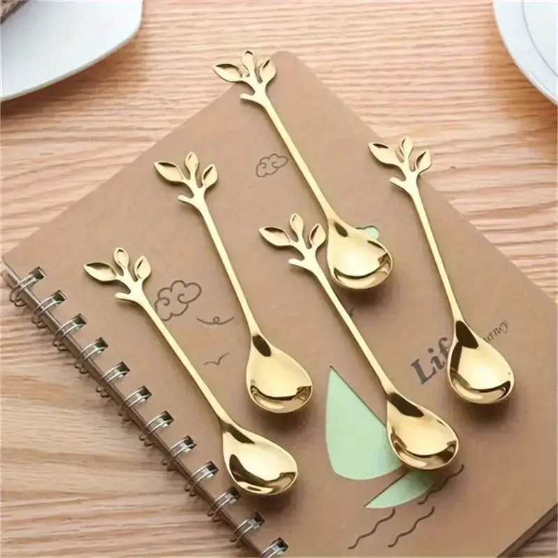 A set of five gold teaspoons with leaf-shaped handles laid out on a notebook.