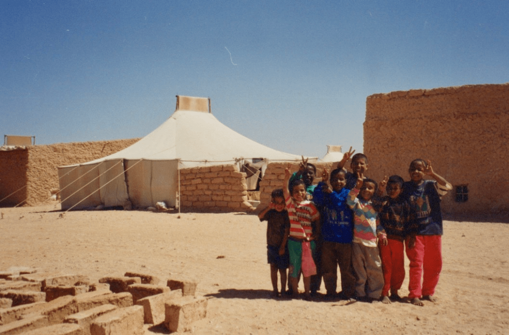 A ggroup of refugee children waving happily outside their tents.