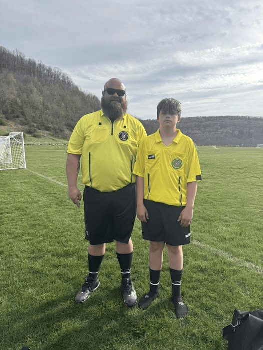 Nelson and a young referee wearing yellow referee uniforms on a soccer field.