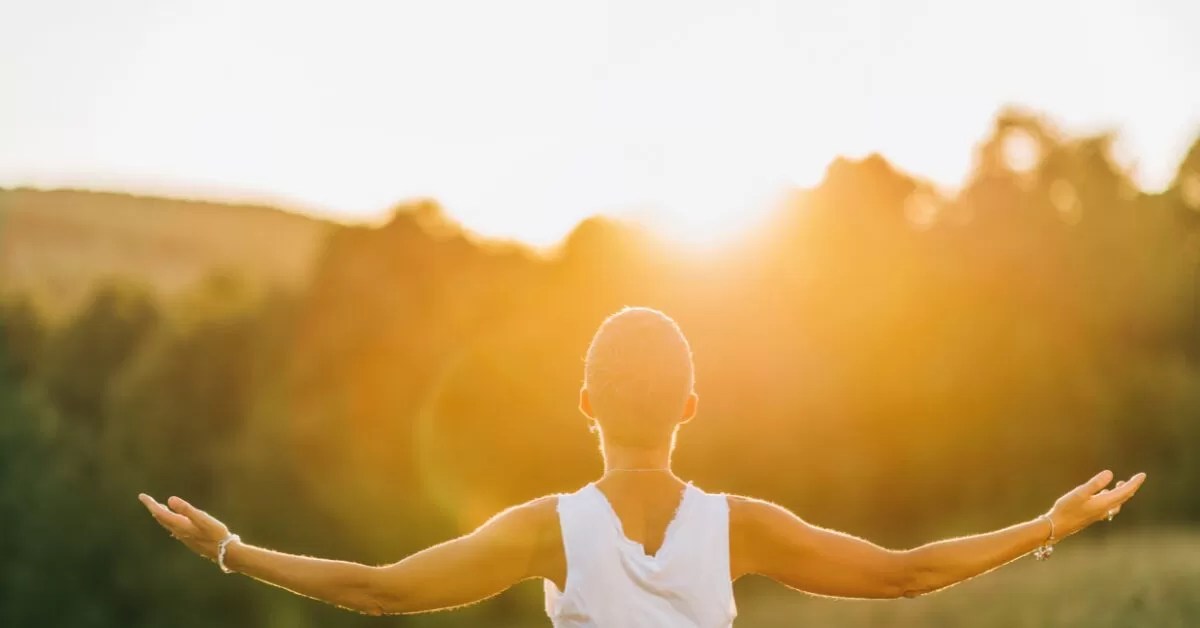 woman seen from behind with arms stretched open wide as the sun sets