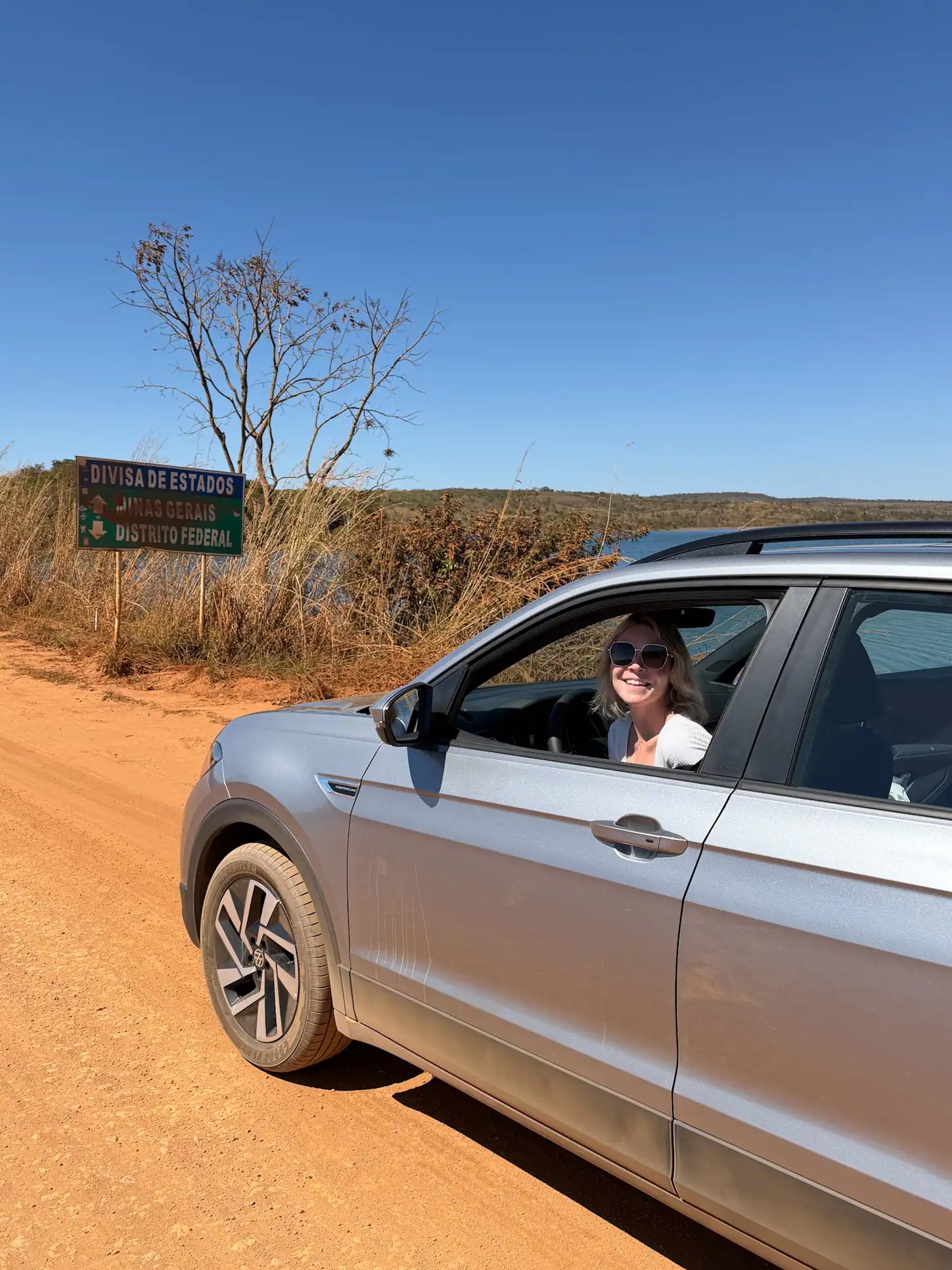 Woman in car near Brasilia border sign on a sunny day. In a Brasilia car rental.