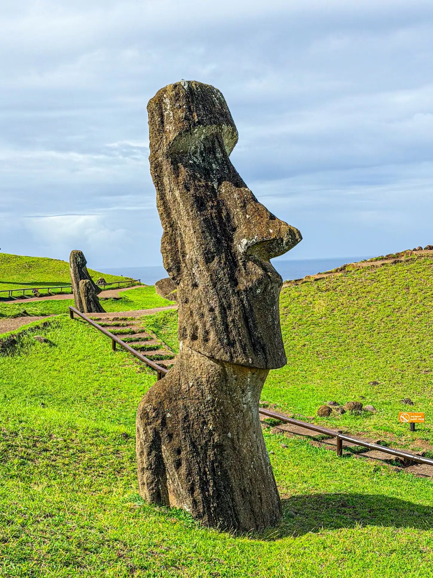 Iconic Moai statue on Easter Island with green landscape and cloudy sky. One of the best things to do on Easter Island.