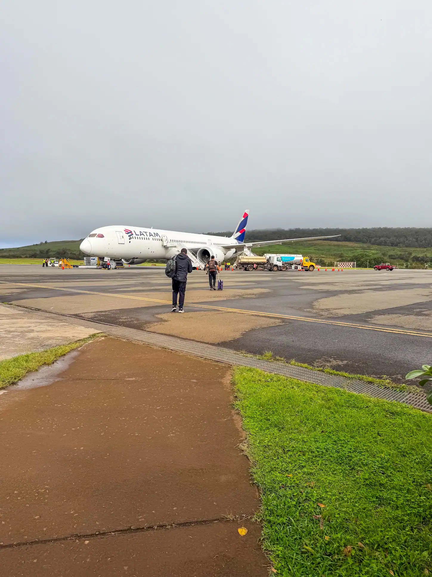 Passenger boarding an airplane at Easter Island airport under cloudy sky.