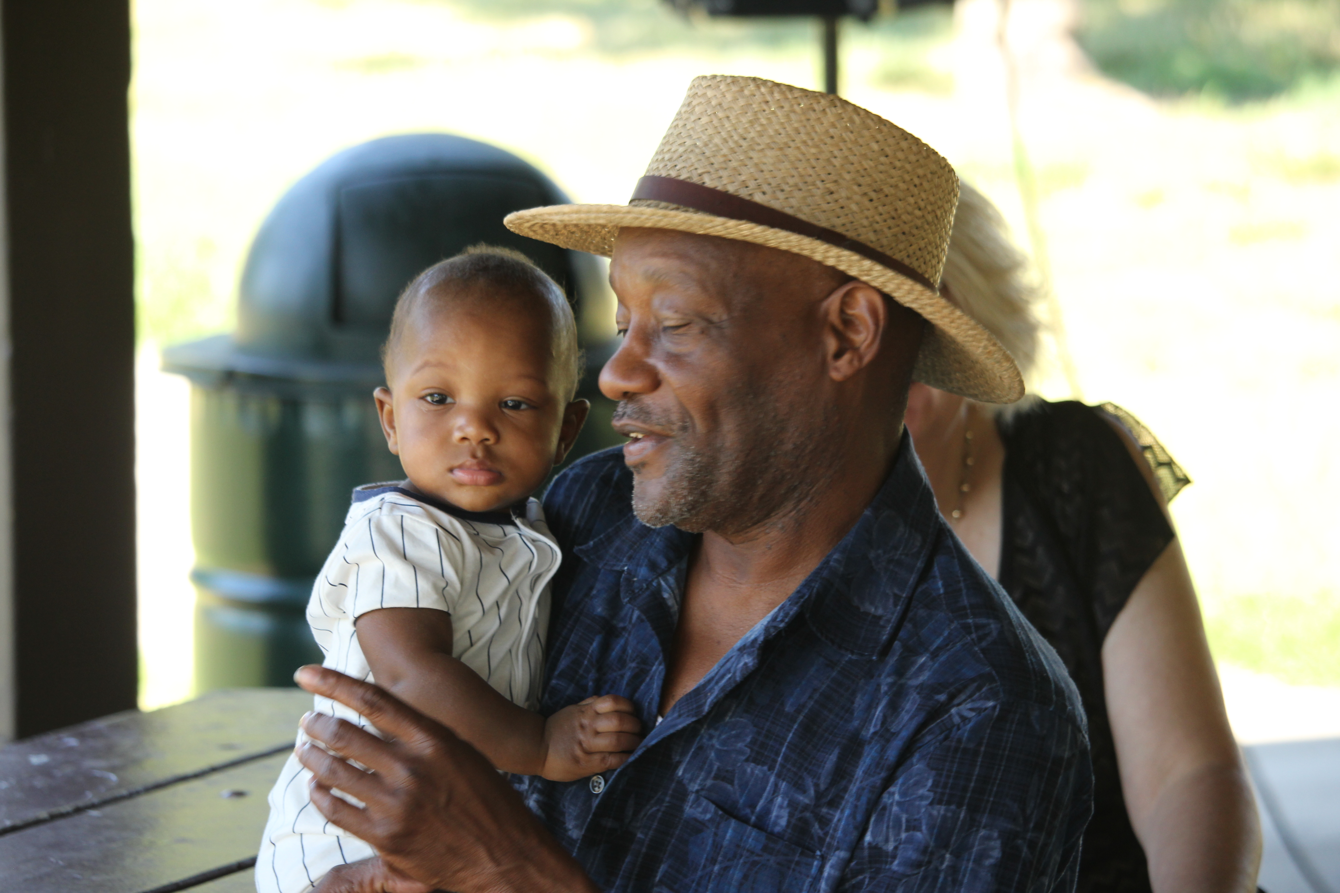 Man wearing light brown hat holding baby