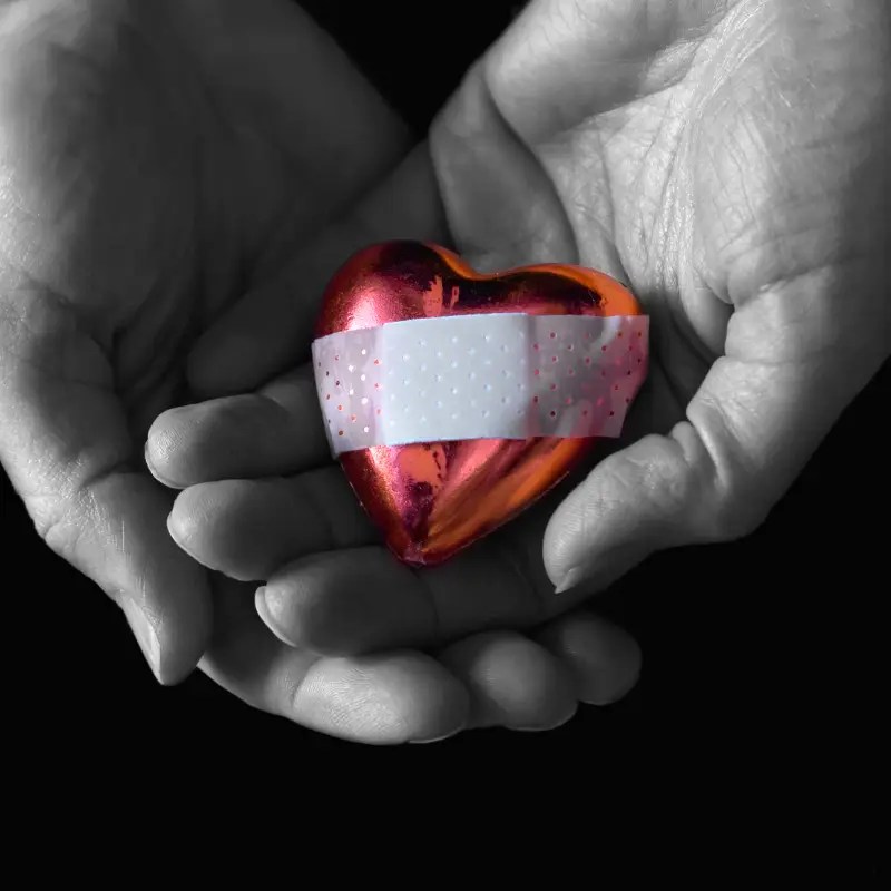 Hands cupped together with a red heart with a band aid on it