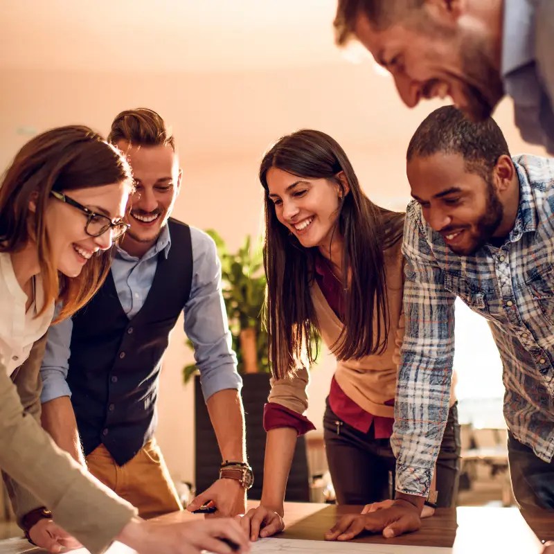 A diverse group of people gathered around a table looking down, appearing to be working on something together