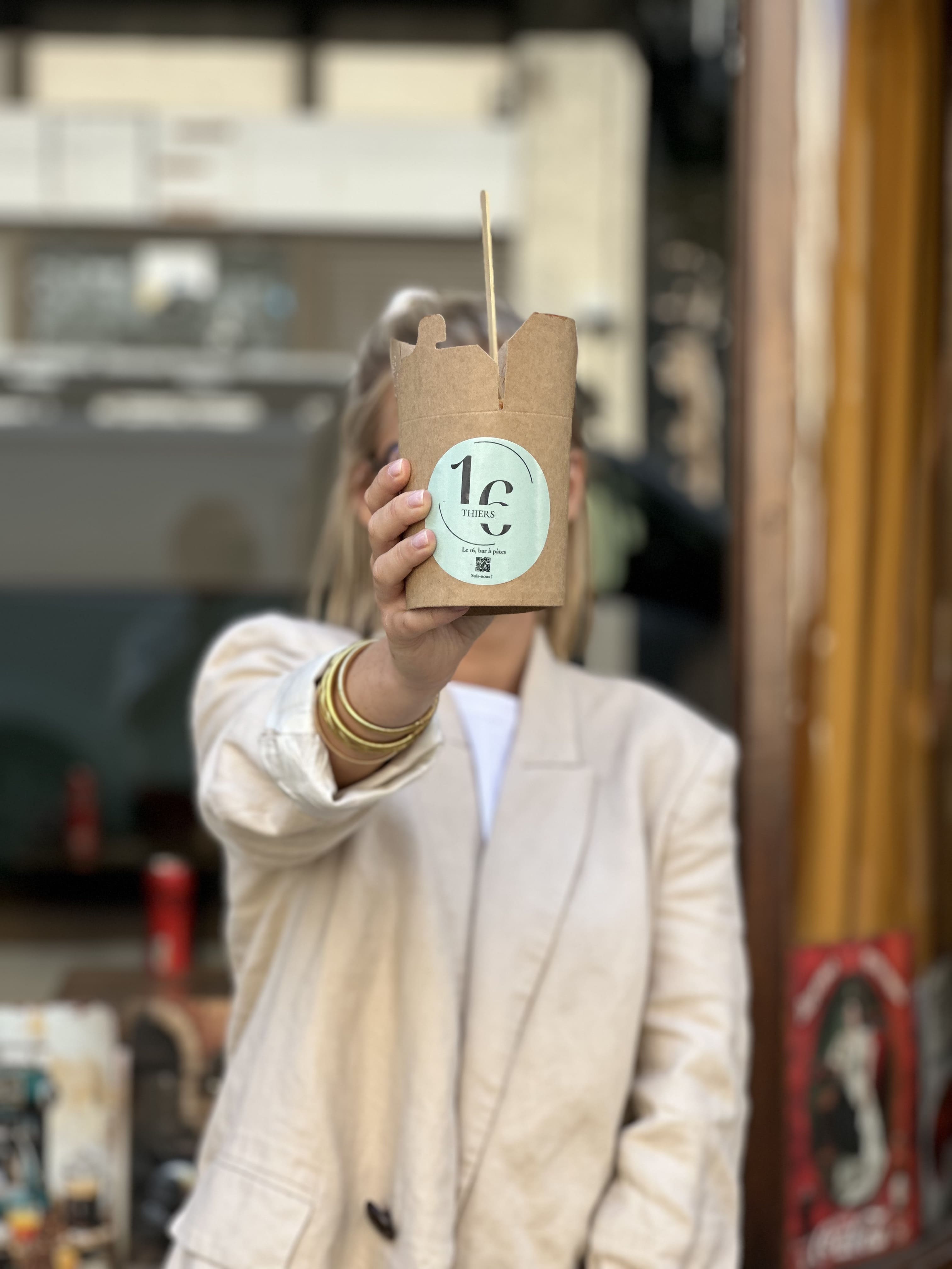 Personne tenant une box de pâtes et cachant son visage.