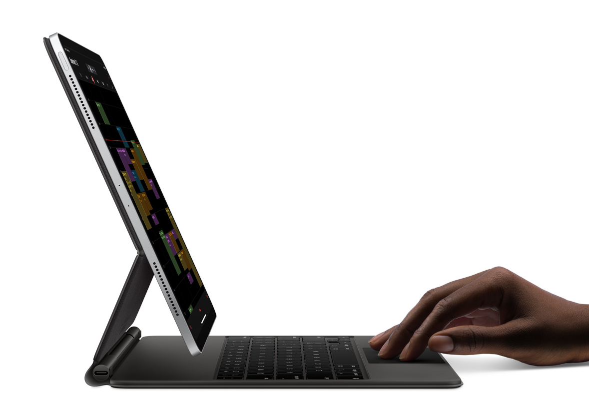 iPad Pro sitting in magic keyboard, floating above it. Large physical keys, a trackpad, and a person's hand on the trackpad, seemingly covering most of the surface area with their four fingers.